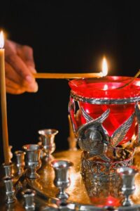 A person lighting candles in front of silver candlesticks.